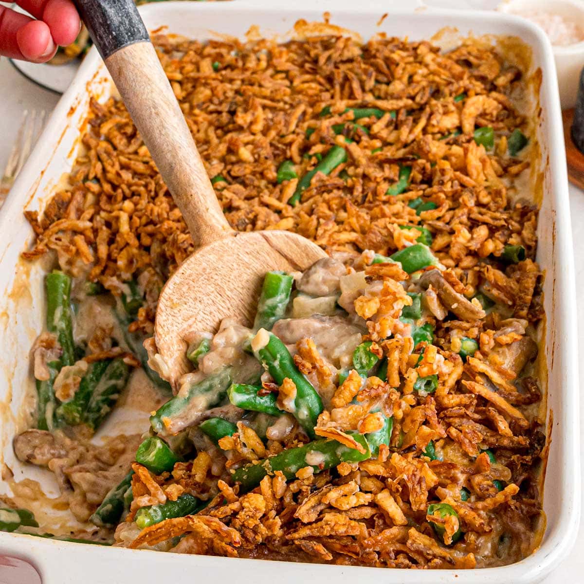 A creamy green bean casserole topped with crispy fried onions in a white baking dish.