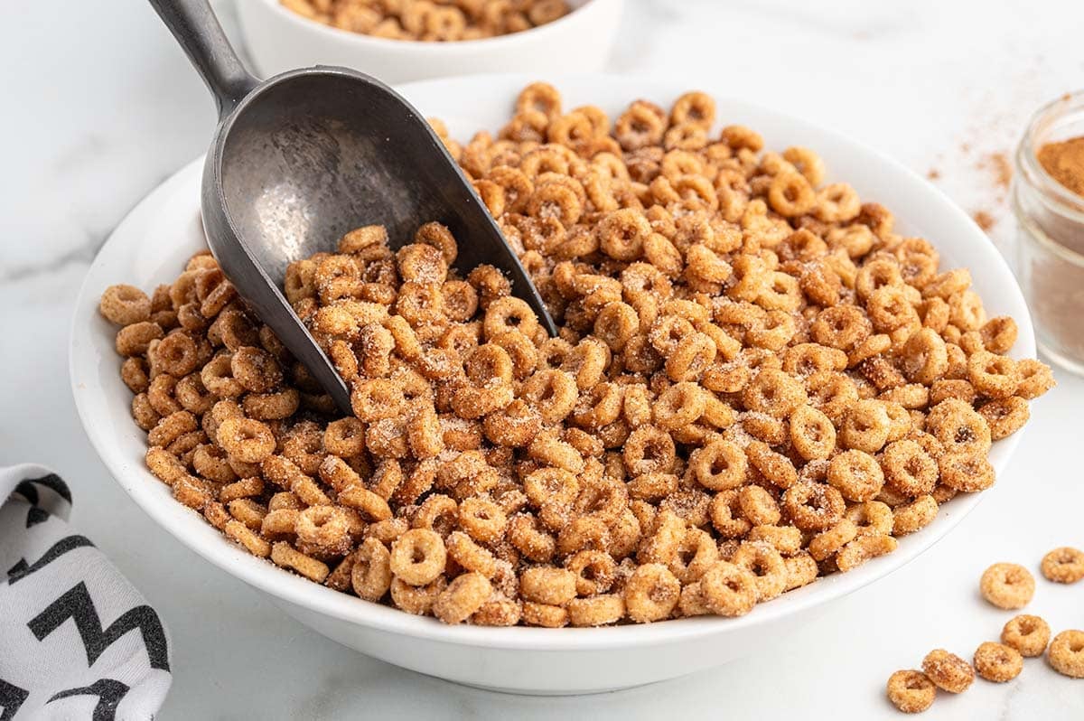 Bowl filled with Mini Donut Hot Buttered Cheerios and a metal scoop inside.