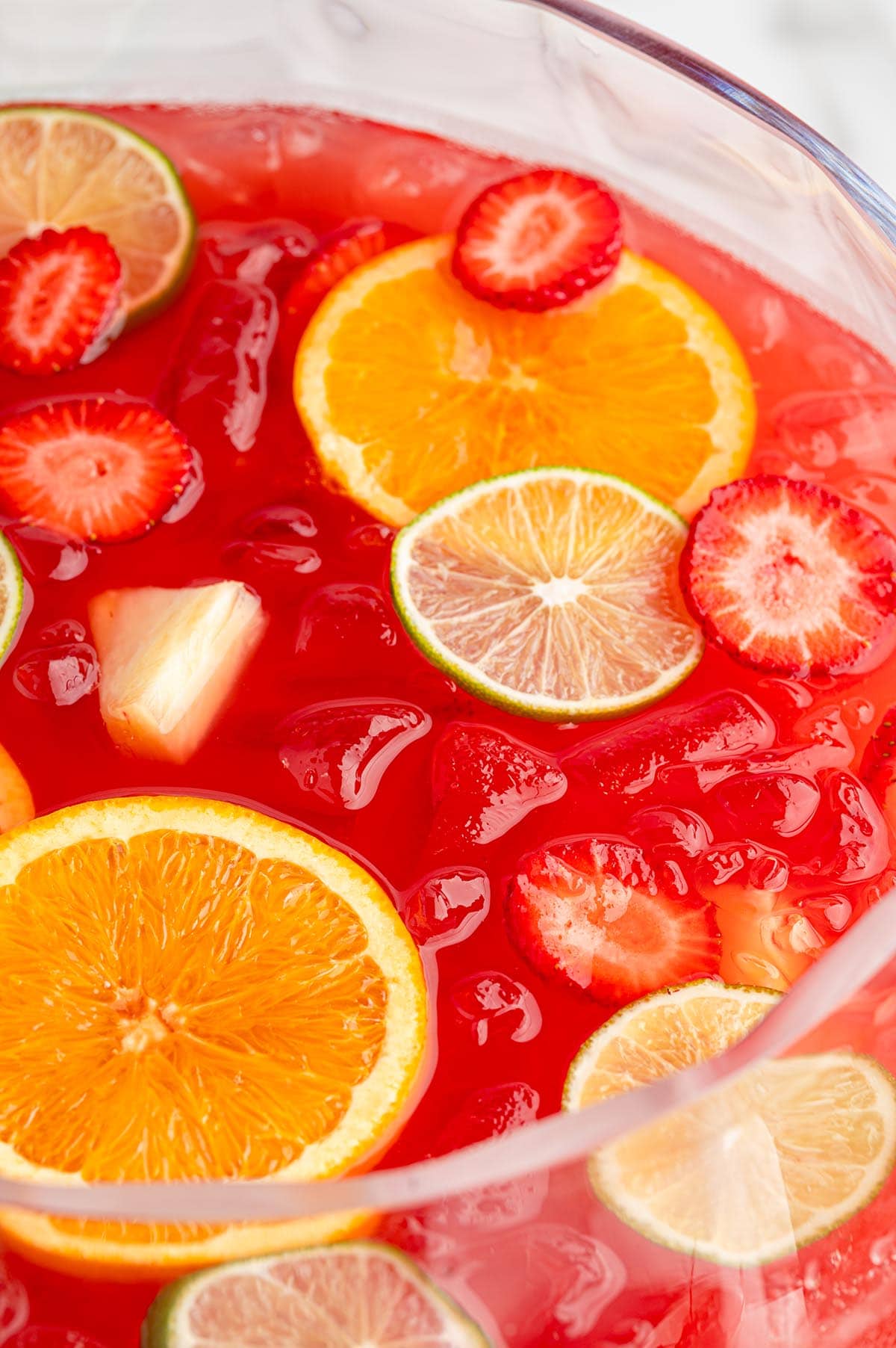 Clear glass bowl filled with red party punch and topped with fresh strawberries, orange slices, and lime wedges.