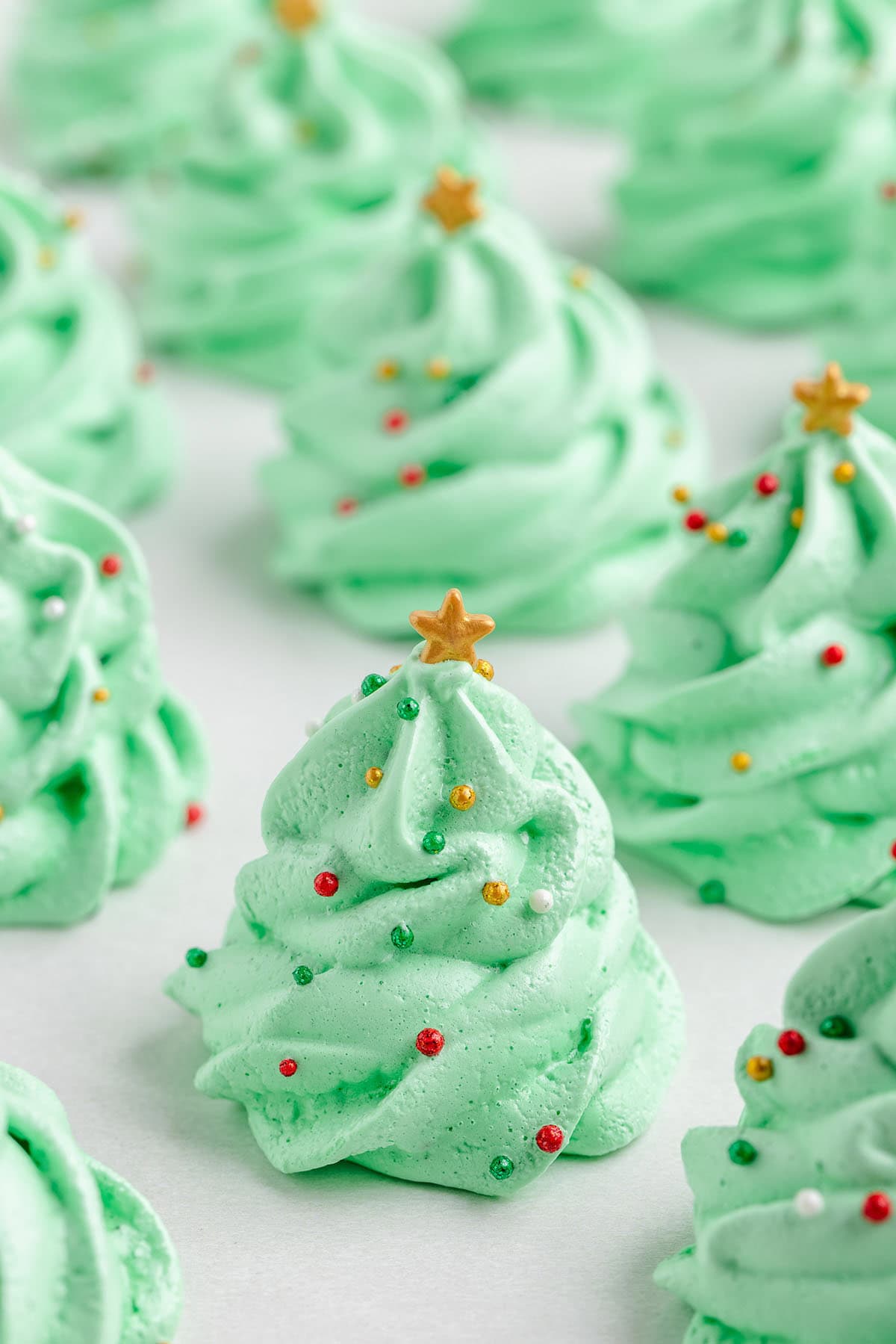 Adorable green Christmas tree meringues on a white plate, featuring shiny gold stars and holiday sprinkles.