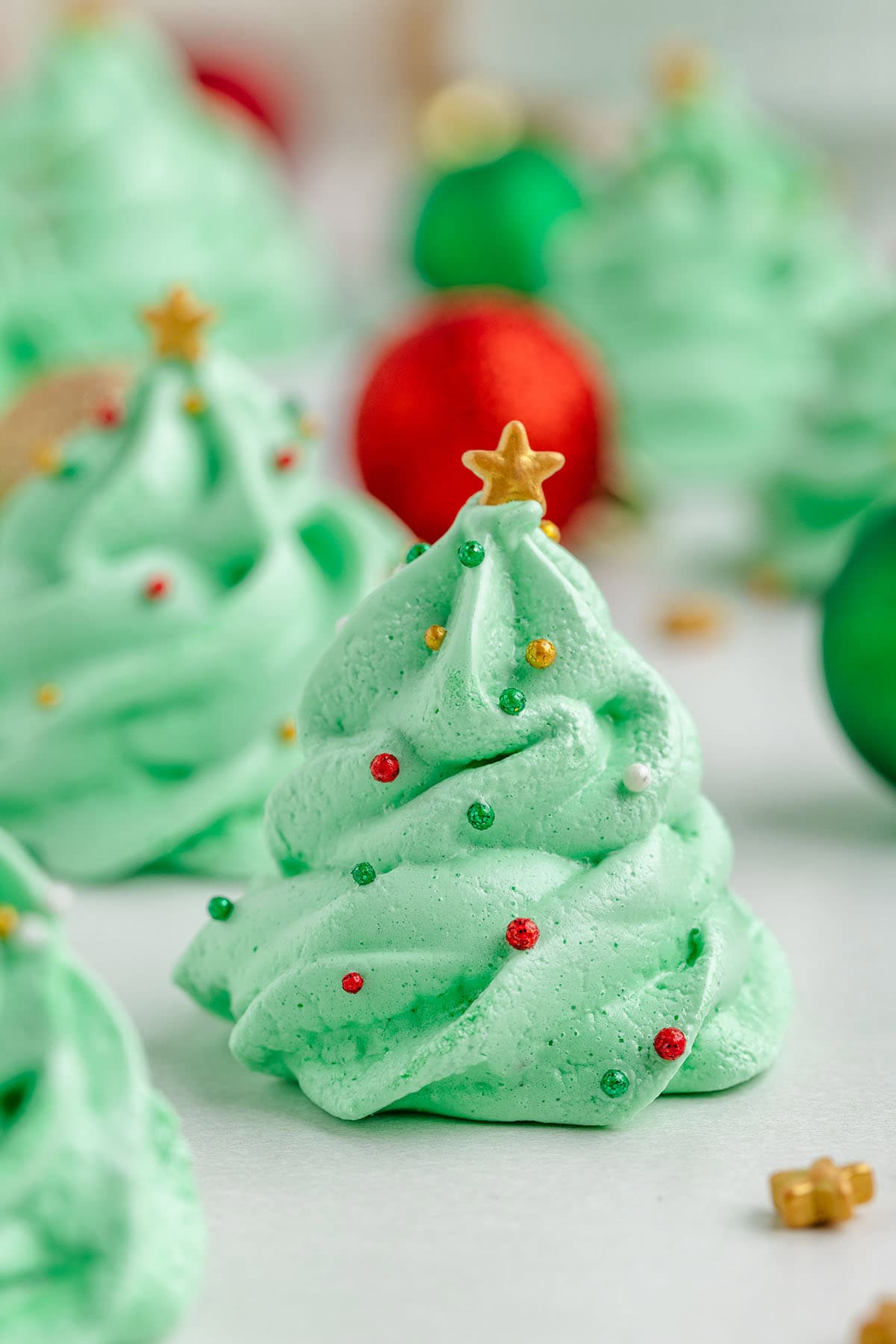 Christmas Tree Meringues cookies shaped like Christmas trees with gold stars and red balls on top.