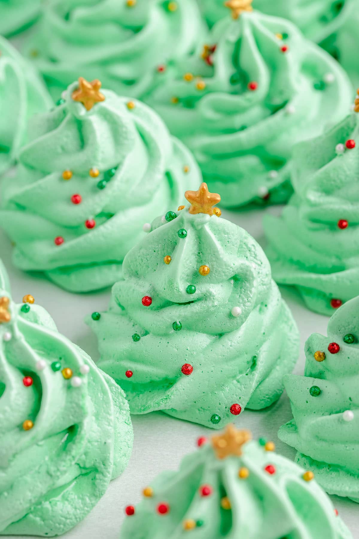 Close-up view of adorable green meringue Christmas trees decorated with gold stars and holiday sprinkles.