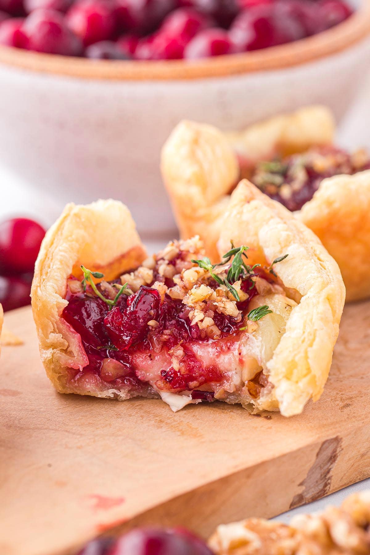 Close-up of cranberry brie bites with fresh cranberries and walnuts on a wooden board.