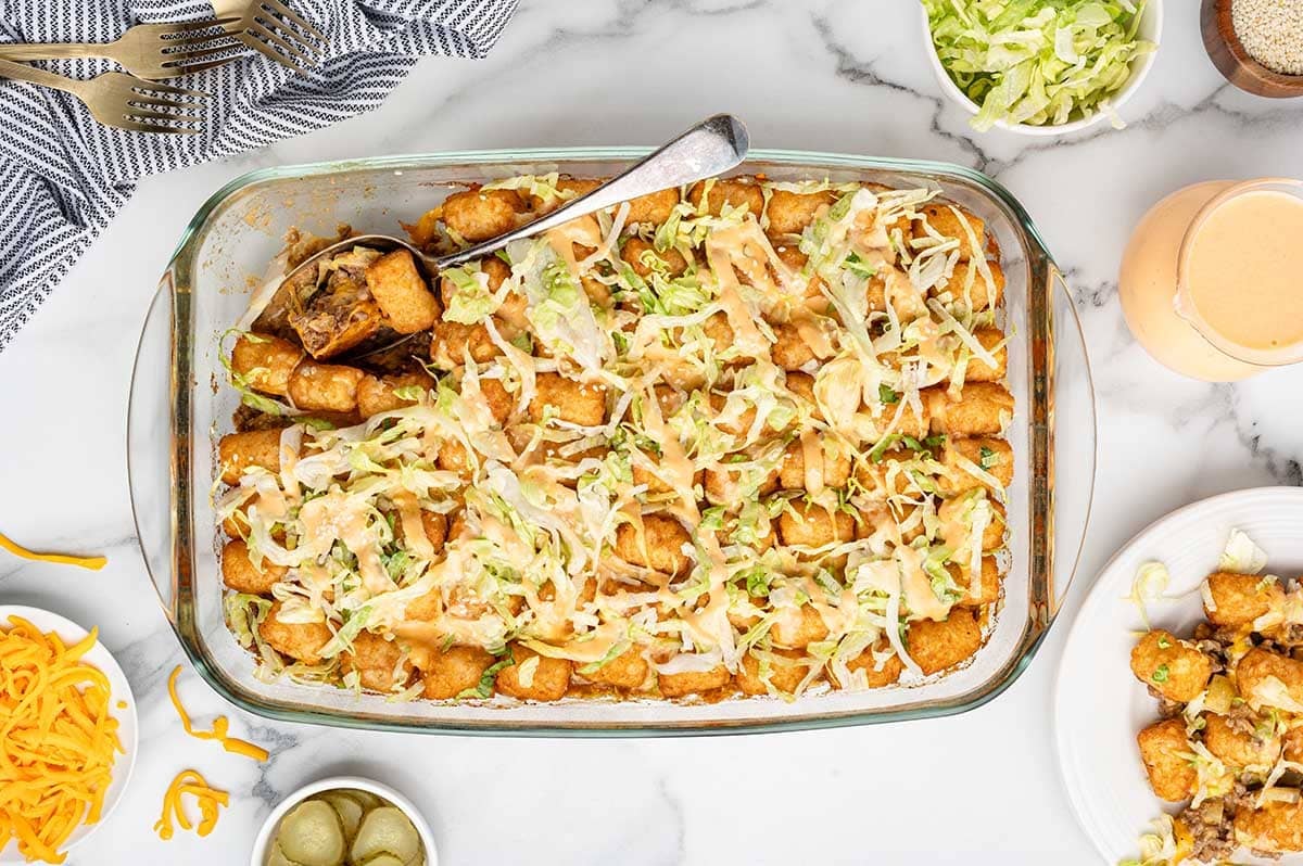 Overhead view of a ready-to-serve Big Mac tatertot casserole with a serving spoon inside the dish.