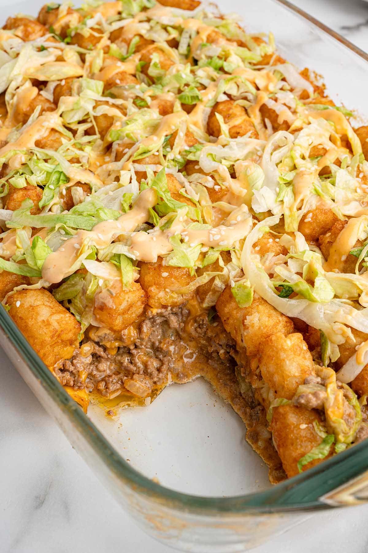A casserole dish filled with Big Mac tatertot casserole topped with shredded lettuce and sauce.