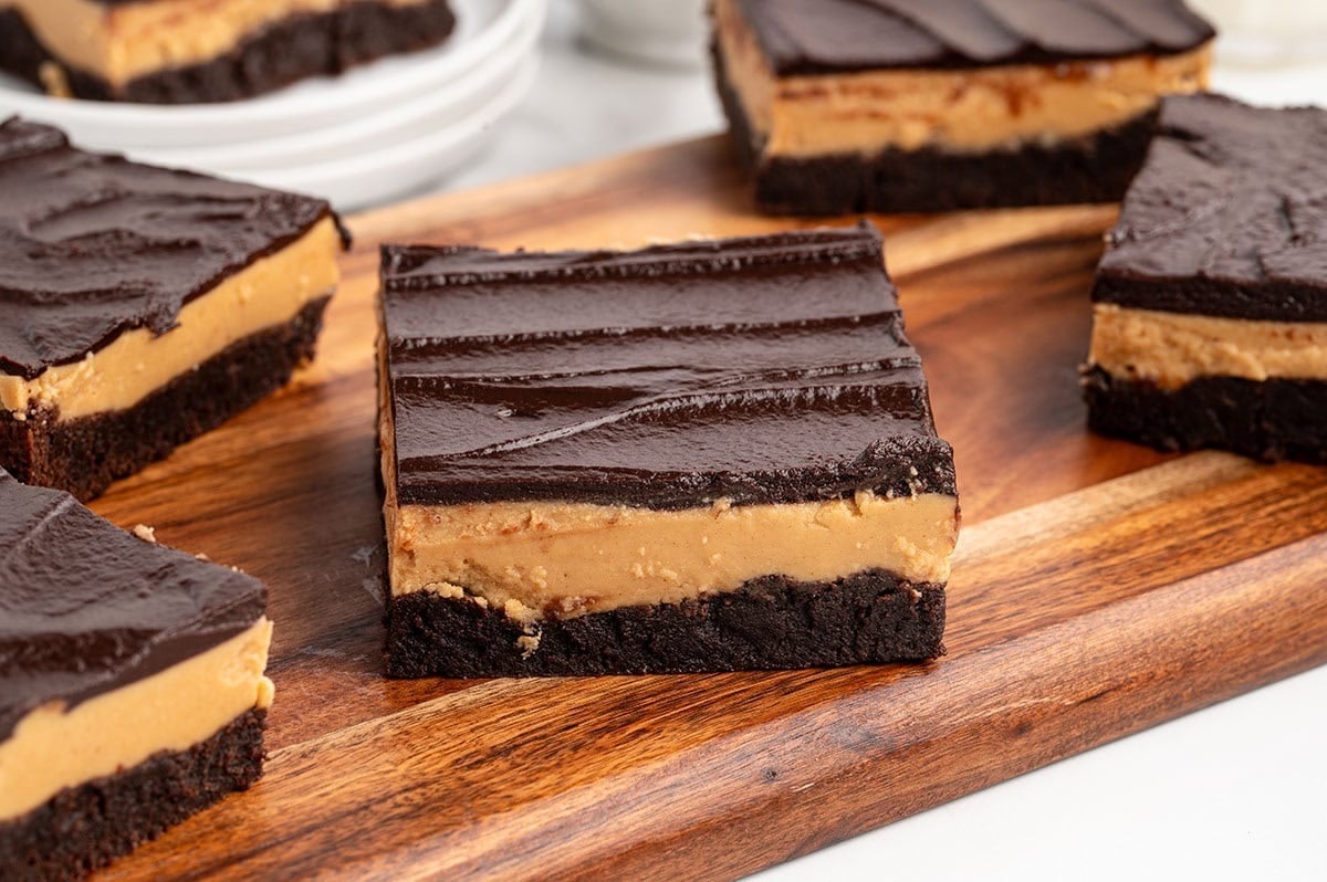 Buckeye brownies topped with chocolate ganache sit on a wooden board.