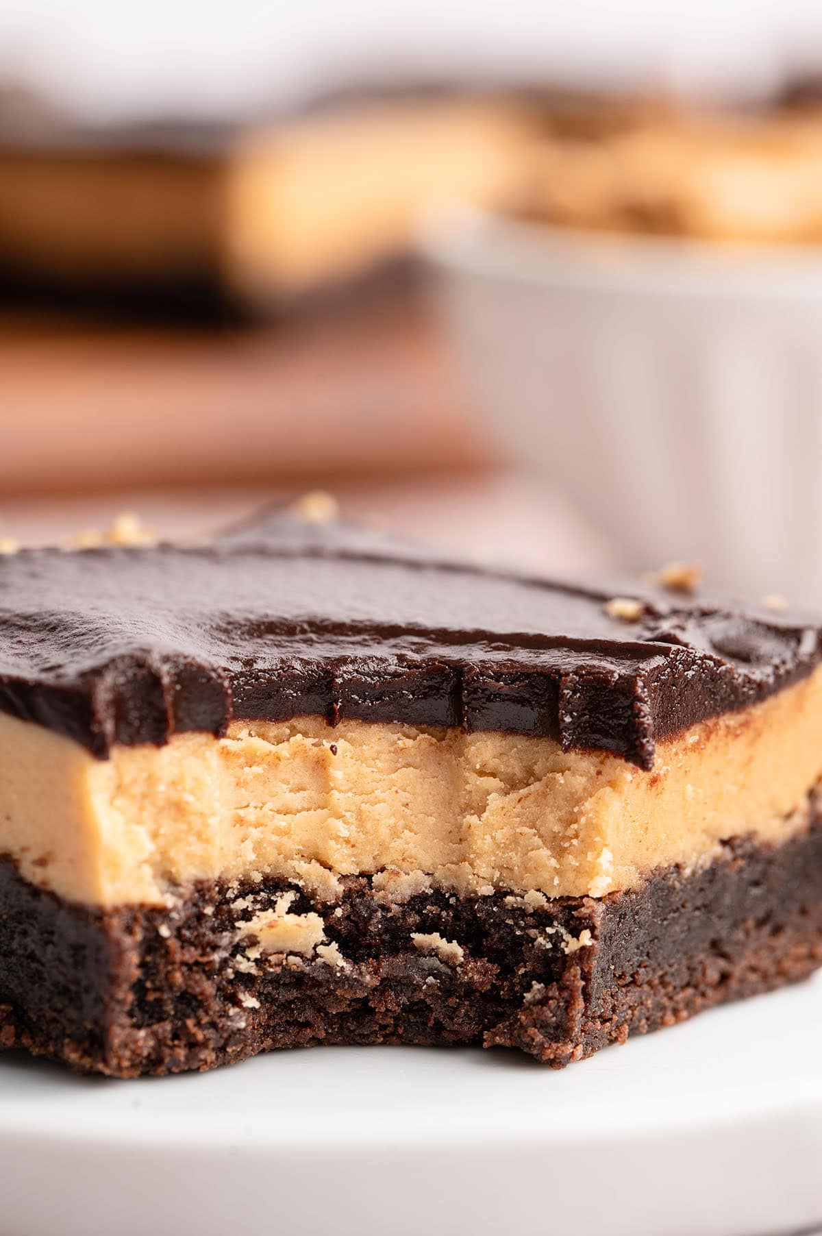 Buckeye brownie square cut to reveal creamy peanut butter center under glossy chocolate, with a chunk missing to show the texture inside.