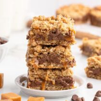 Three stacked caramel oat bars drizzled with gooey caramel on a white plate.