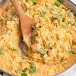cheesy chicken orzo in a skillet with wooden spoon.