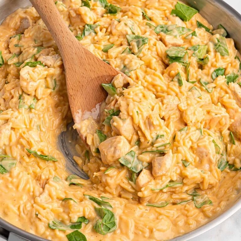 cheesy chicken orzo in a skillet with wooden spoon.