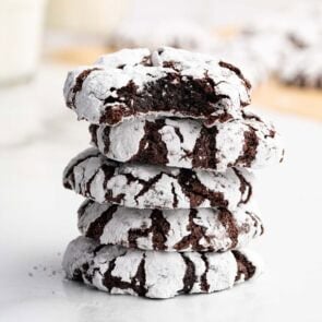 Stack of chocolate crinkle cookies dusted with powdered sugar, one shows a bite revealing the rich chocolate center.