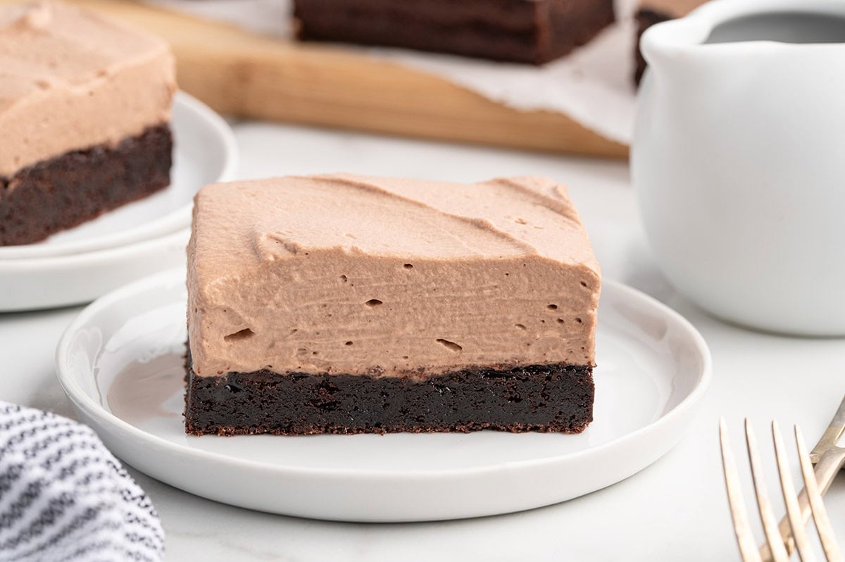 Chocolate mousse brownies with thick topping beside a pitcher of cream.