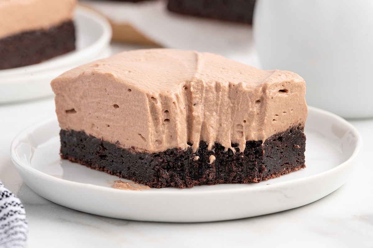 A slice of chocolate mousse brownies on a white plate, topped with thick mousse and a bite taken out.