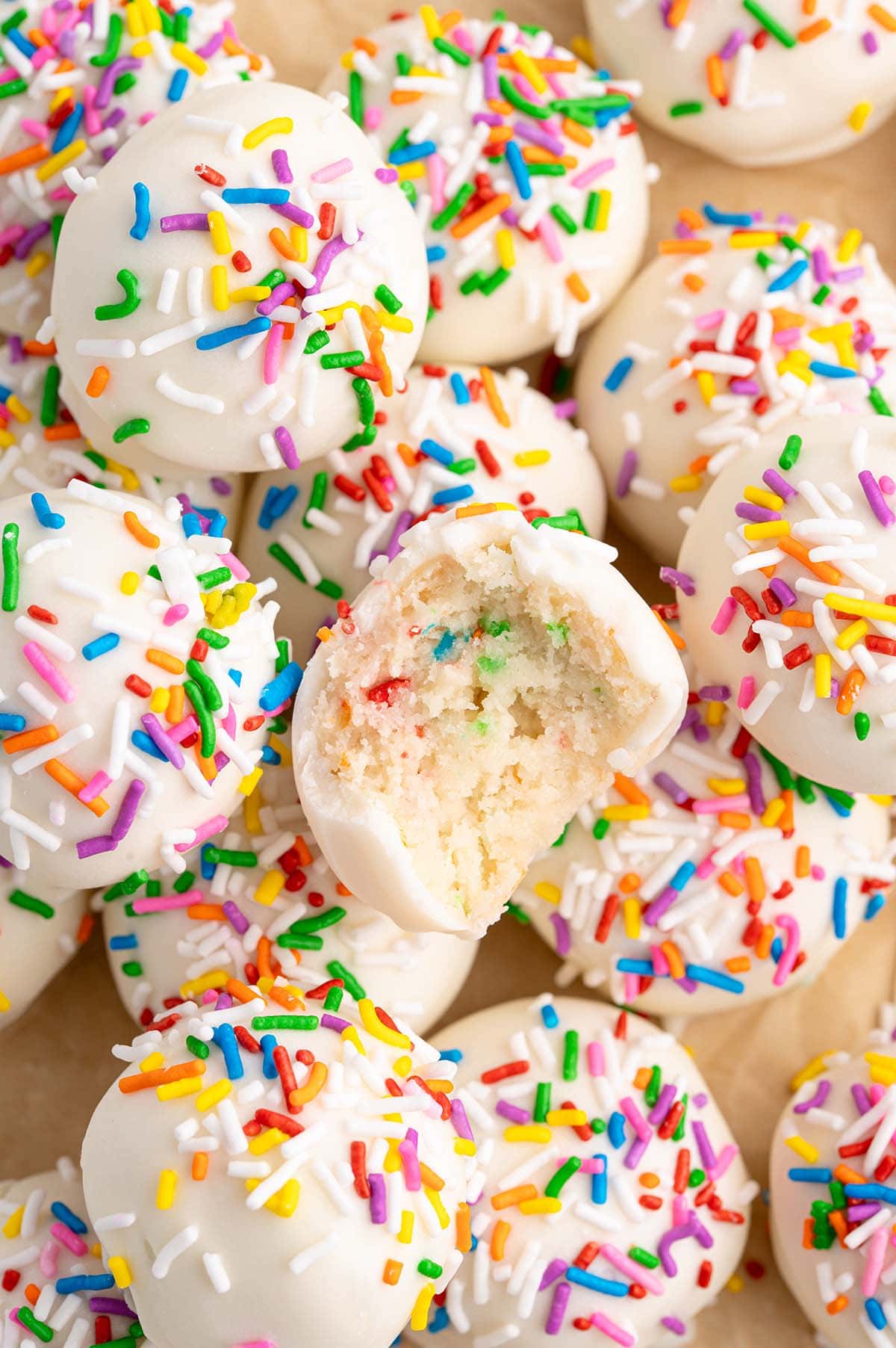 Bite-sized cheesecake balls treats dipped in white almond bark with rainbow sprinkles.