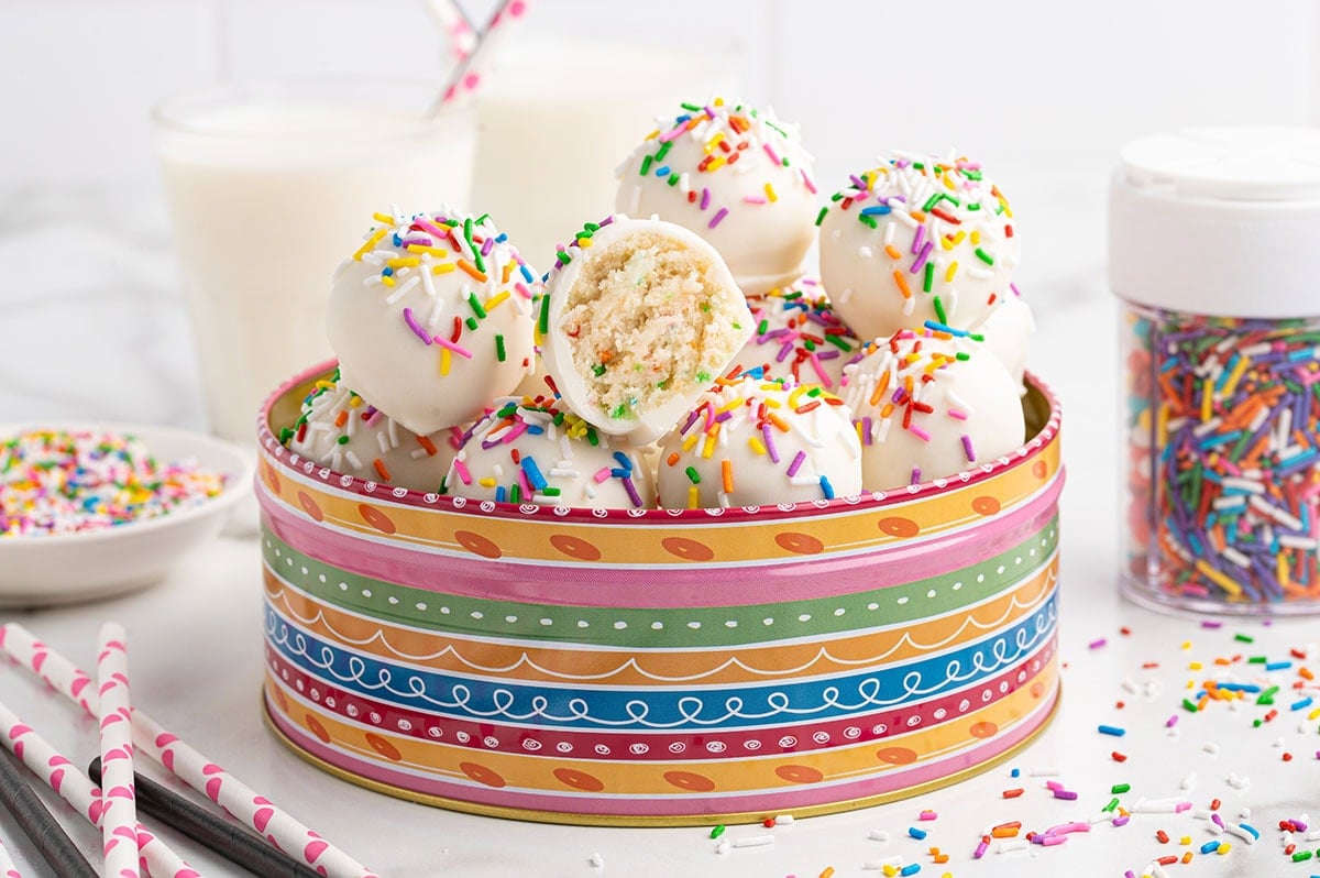 Colorful sprinkle-topped cheesecake balls ready to enjoy with a glass of milk in the background.