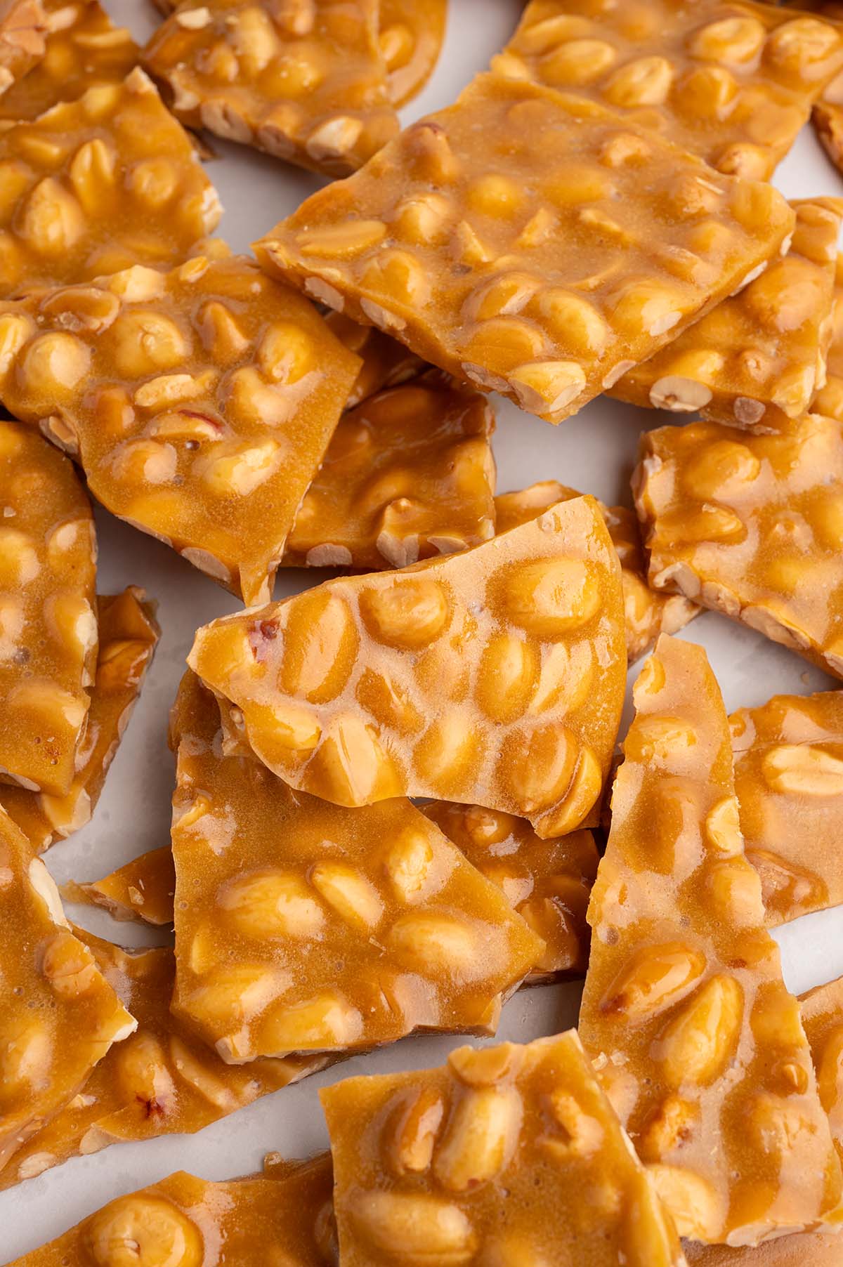 Close-up of golden peanut brittle pieces scattered on a white surface.