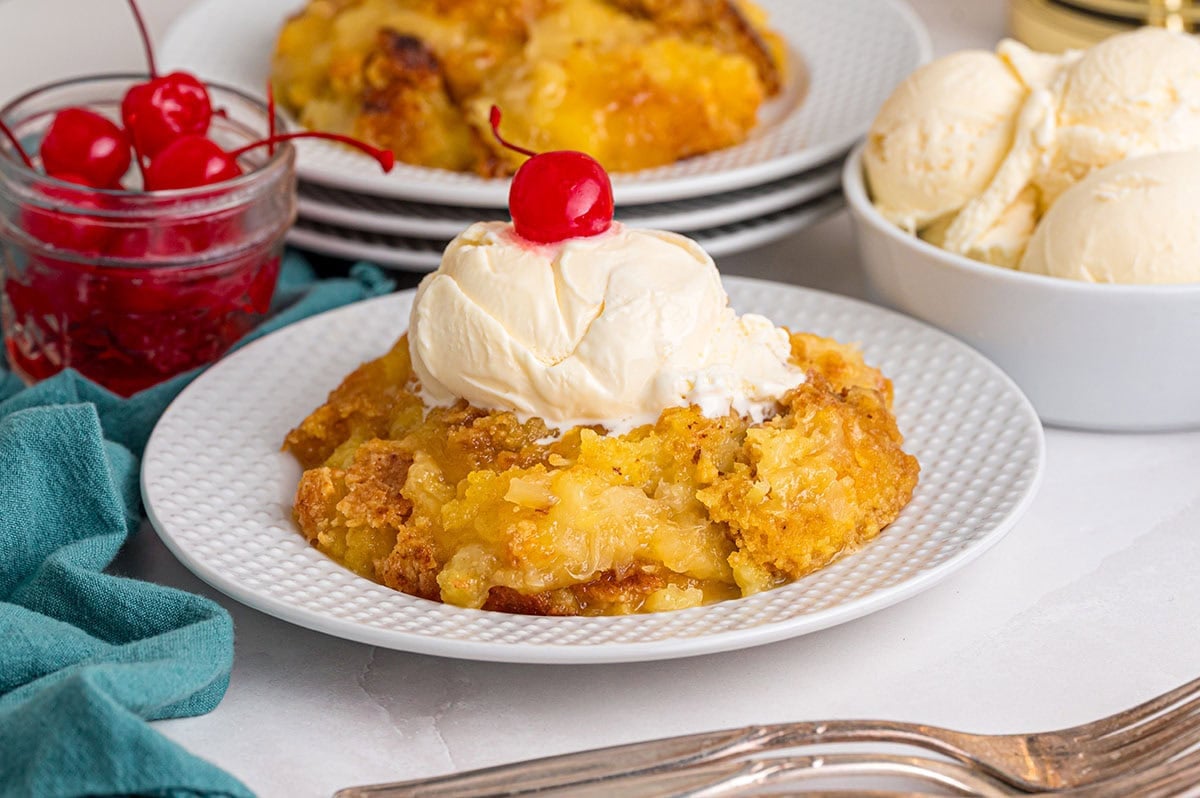 A plate with pineapple dump cake topped with a scoop of vanilla ice cream and a cherry.