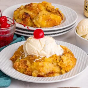 A slice of pineapple dump cake topped with vanilla ice cream and a cherry.