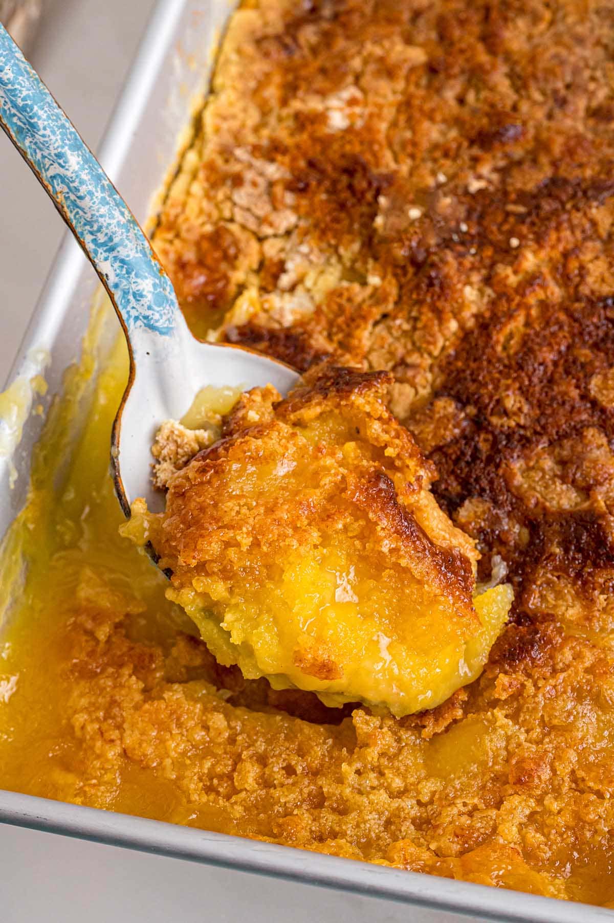 A close-up of a golden pineapple dump cake in a metal pan with a serving spoon.