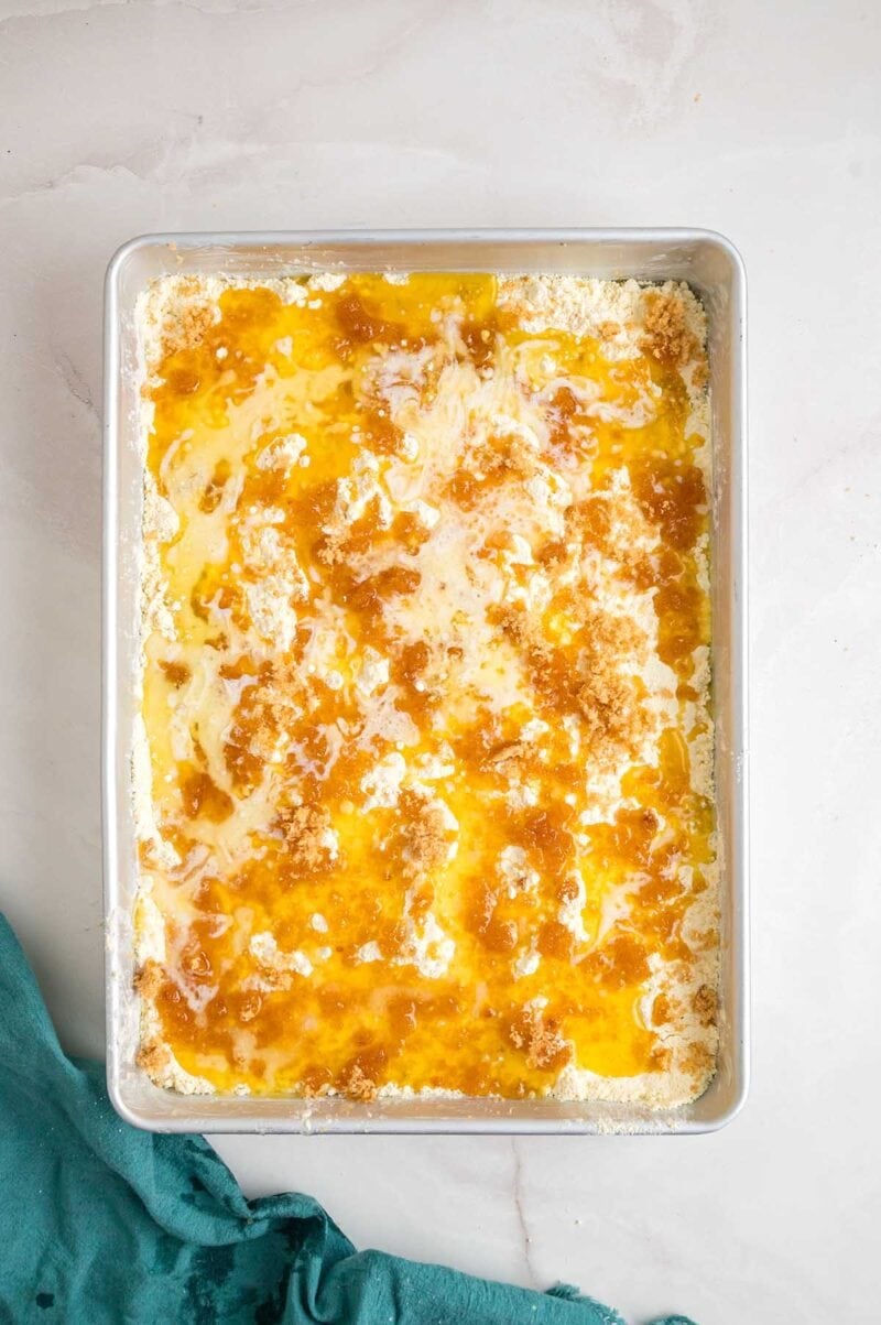 crushed pineapple topped with cake mix followed by melted butter in baking pan