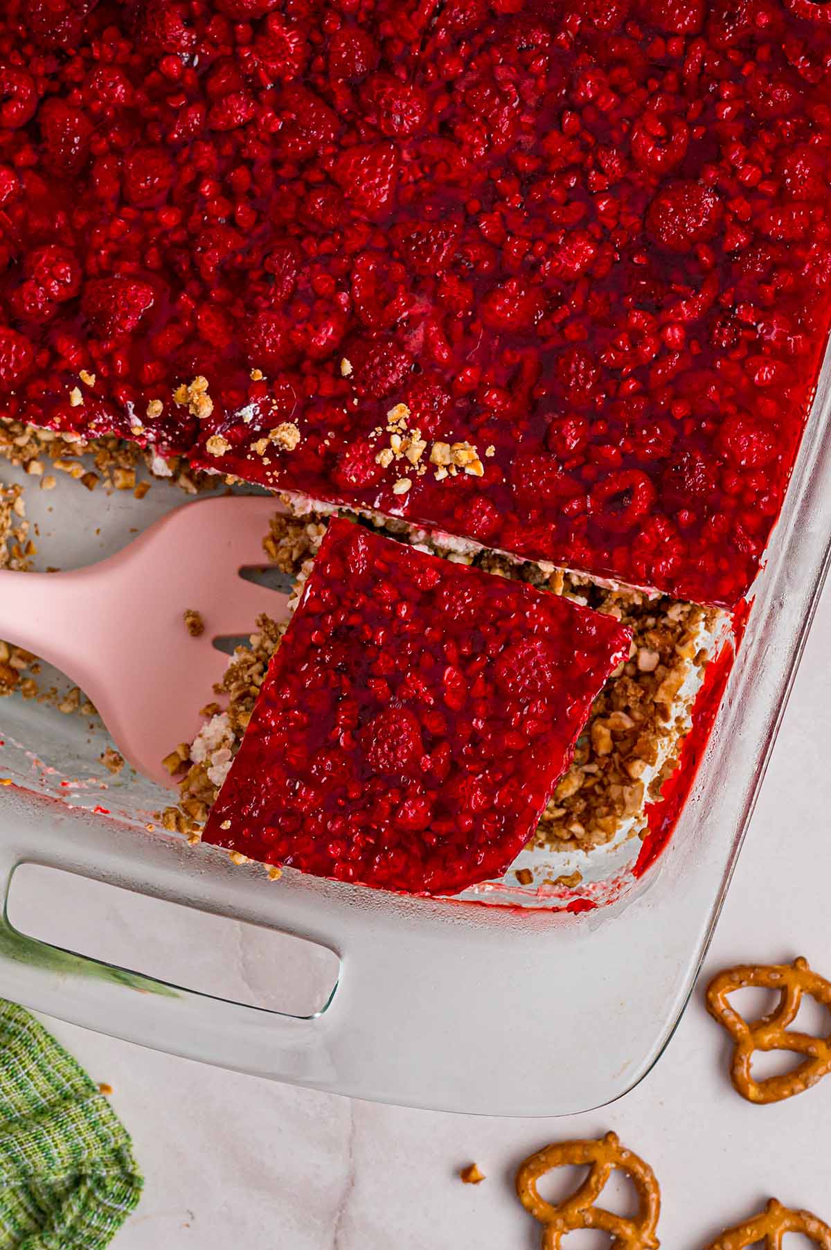 Close up view of a spatula digging into a slice of raspberry pretzel salad in a baking dish