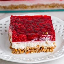 A square slice of raspberry pretzel salad on a white plate.