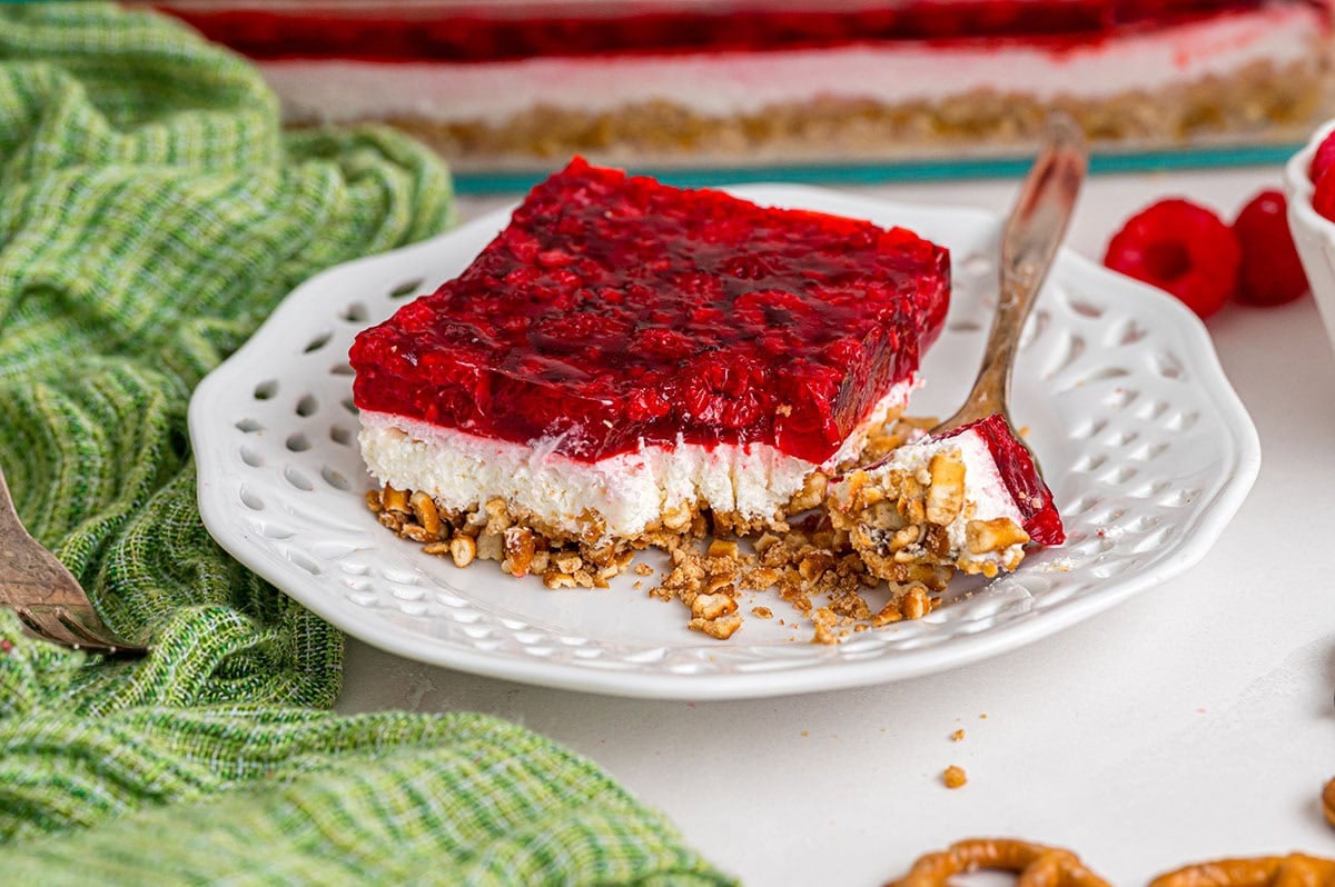 A slice of raspberry pretzel salad on a white plate with a bite taken out.
