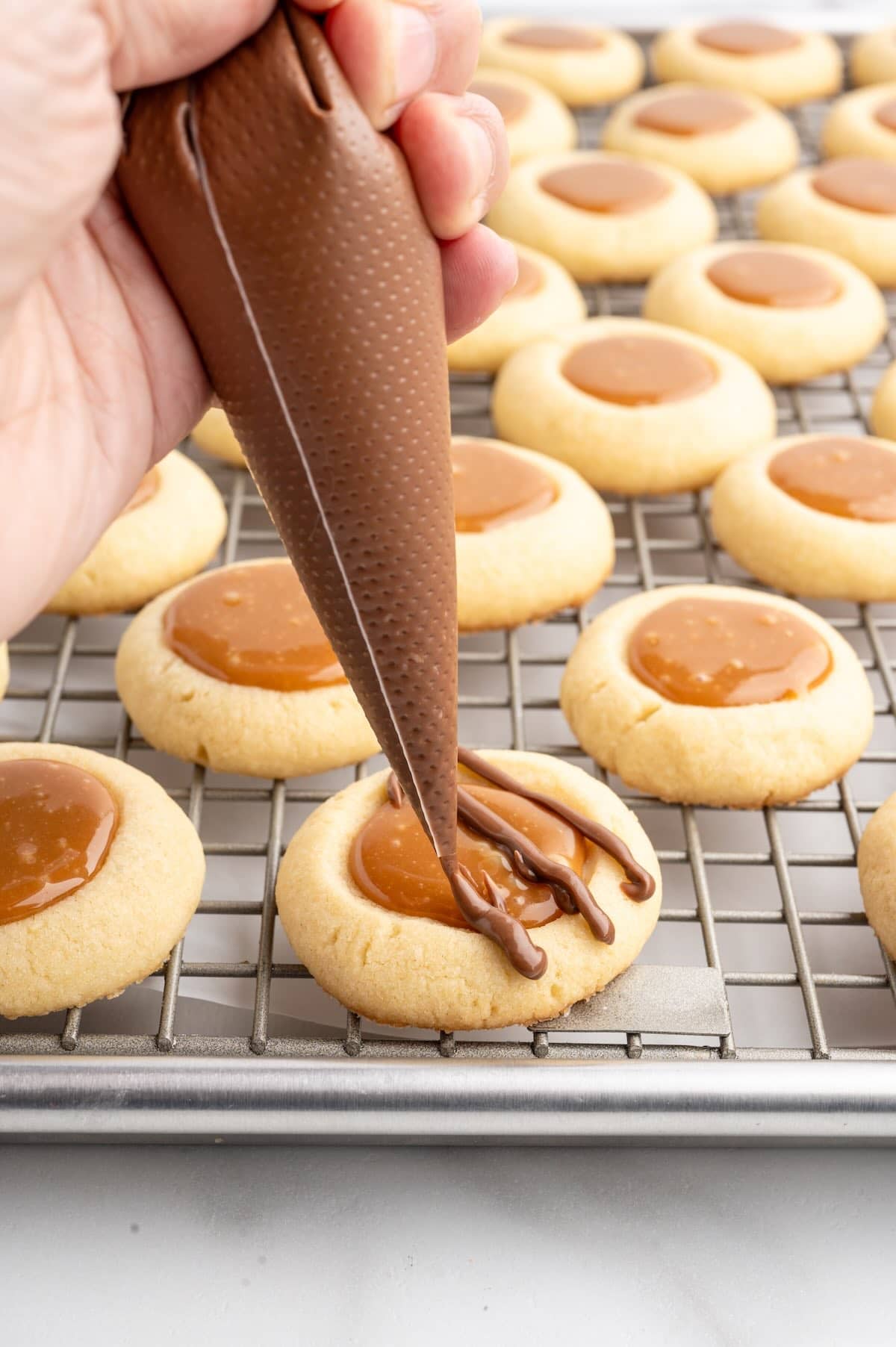 drizzling melted chocolate on baked Twix thumbprint cookies