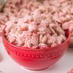 Red bowl full of pink Candy Cane Muddy Buddies Chex Mix with crushed peppermint bits.