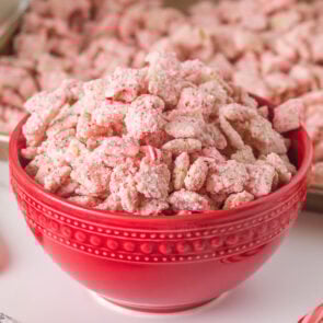 Red bowl full of pink Candy Cane Muddy Buddies Chex Mix with crushed peppermint bits.