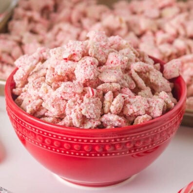 Red bowl full of pink Candy Cane Muddy Buddies Chex Mix with crushed peppermint bits.
