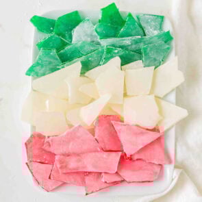 Colorful hard candy shards in green, white, and pink sit on a white plate.
