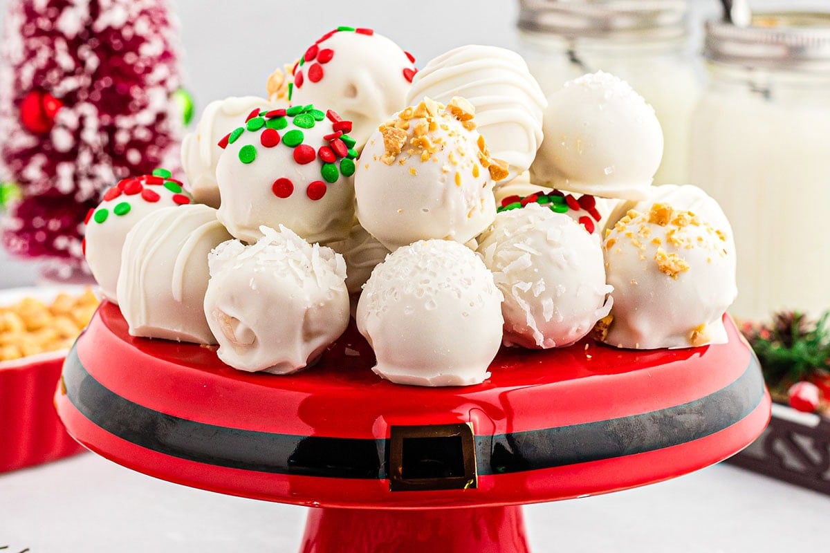 White chocolate Christmas truffles topped with red and green sprinkles sit on a red Santa belt plate.