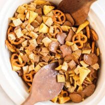 A white bowl holds a fresh batch of Crockpot Chex Mix with crunchy Chex cereal, pretzels, and nuts.
