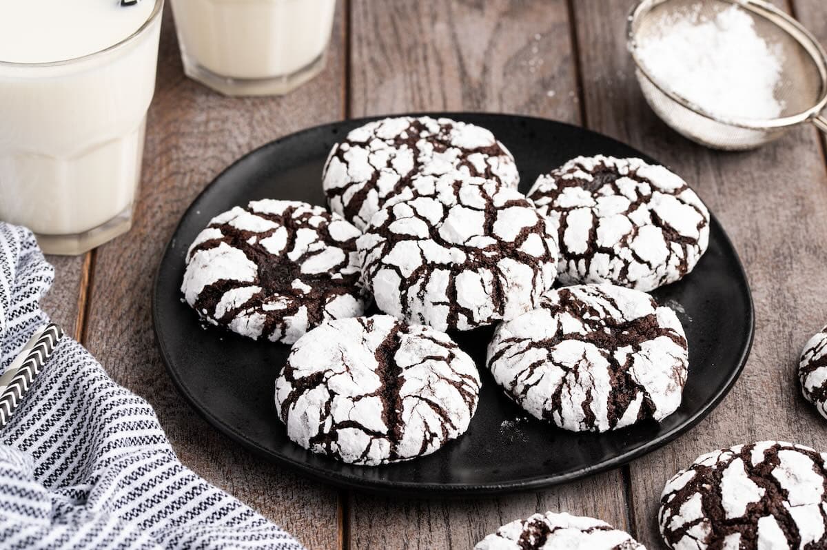 chocolate crinkle cookies stacked on a black plate on top of wooden table.