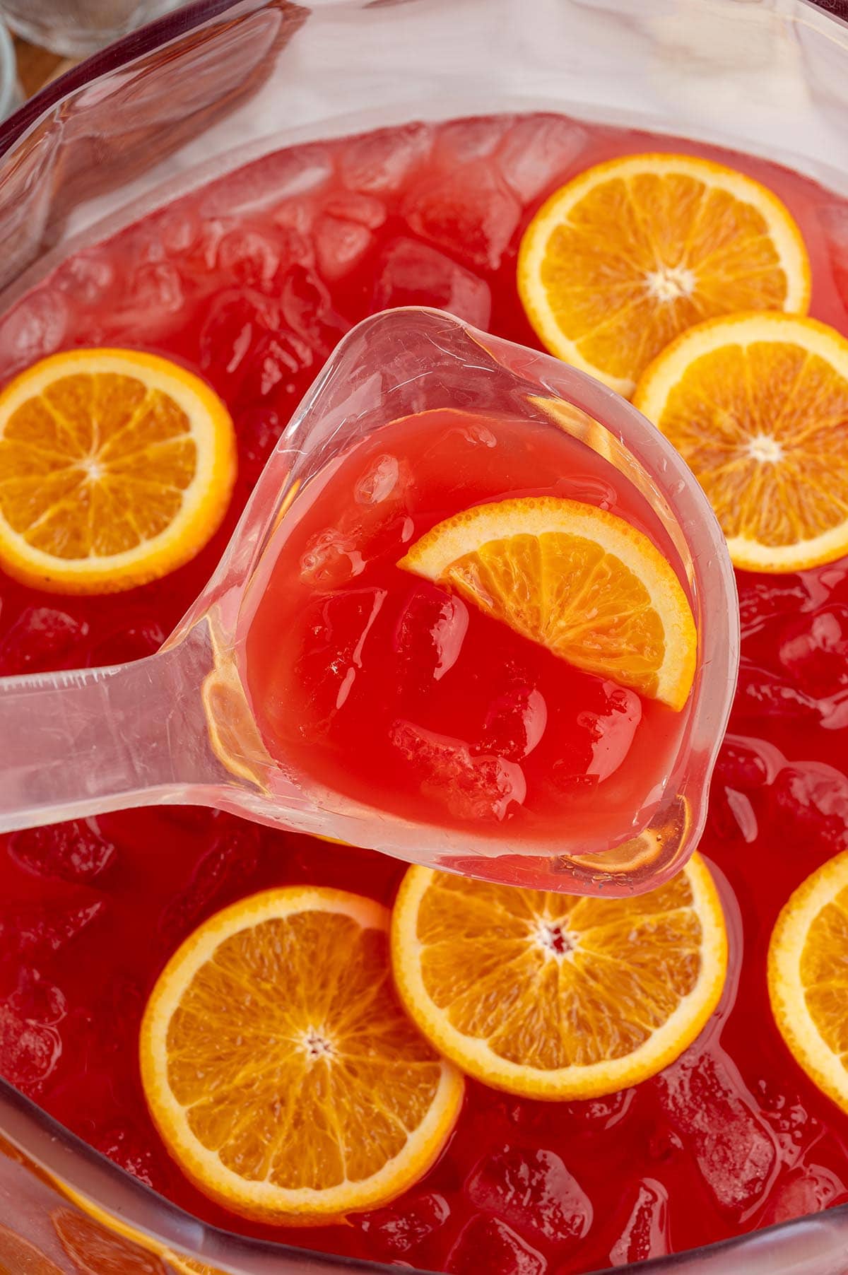 Ladle scoops red punch from a bowl garnished with fresh orange slices and ice.