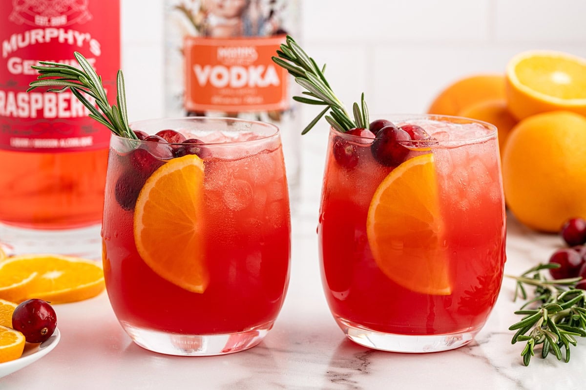 Two glasses of red Christmas Morning Punch topped with orange slices and cranberries.
