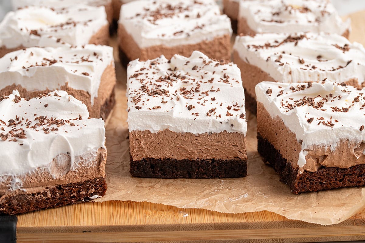 Sliced French silk brownies with rich chocolate base and creamy white topping on a wooden board.