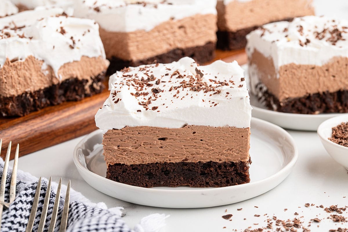 A slice of French silk brownie with chocolate base, smooth mousse, and whipped cream topping on a white plate.