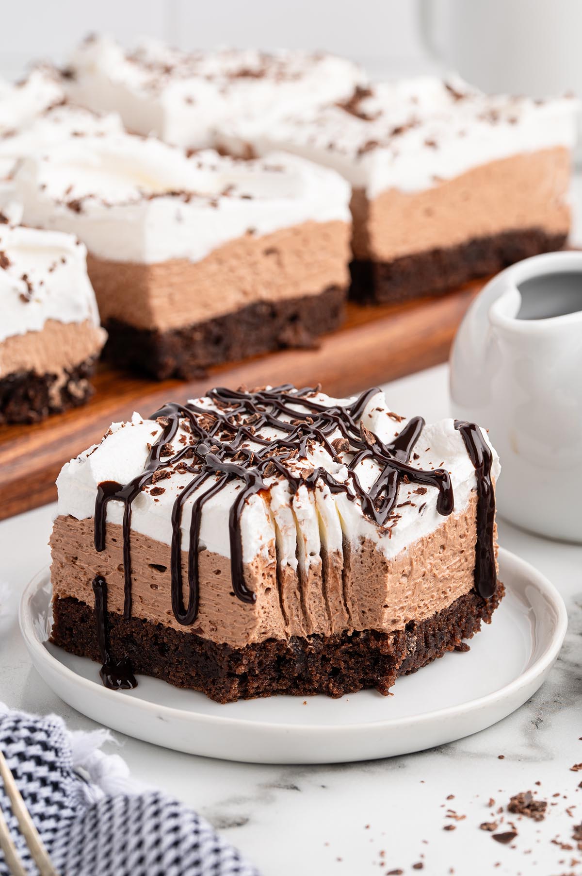 A close-up slice of French silk brownie with chocolate layers and whipped cream topping on a white plate.