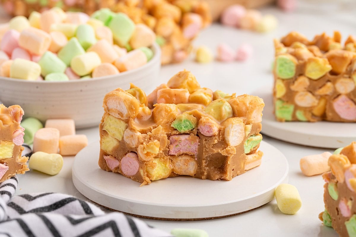A close-up of a peanut butter marshmallow square with a bite missing, showing colorful marshmallows and cereal bits.