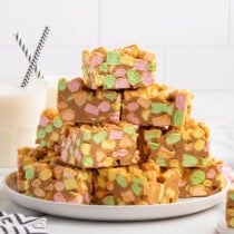 Stack of colorful peanut butter marshmallow squares on a white plate next to a glass of milk.