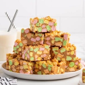 Stack of colorful peanut butter marshmallow squares on a white plate next to a glass of milk.