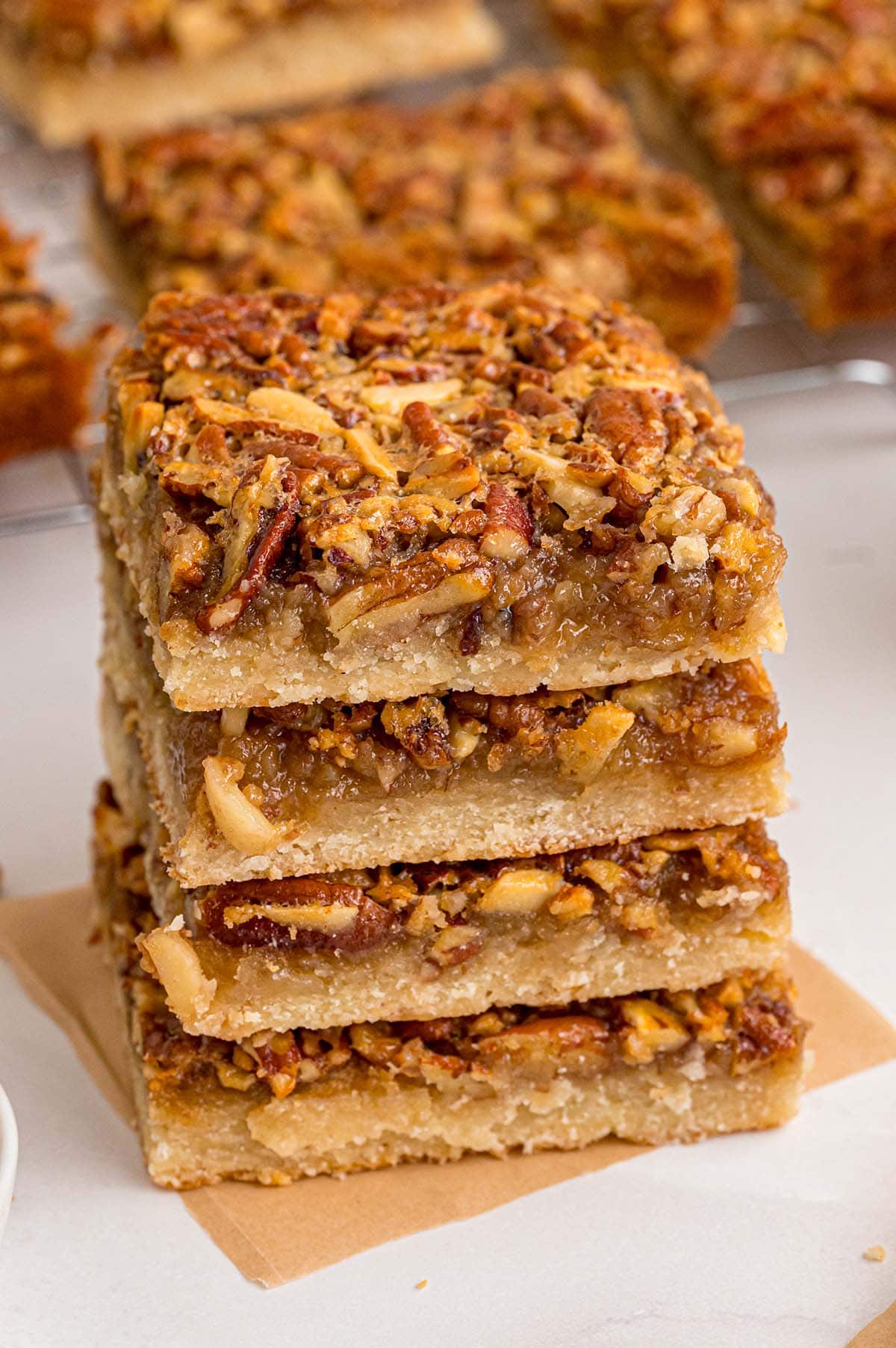 Fresh pecan pie bars with sticky filling and whole pecans cooling on parchment.
