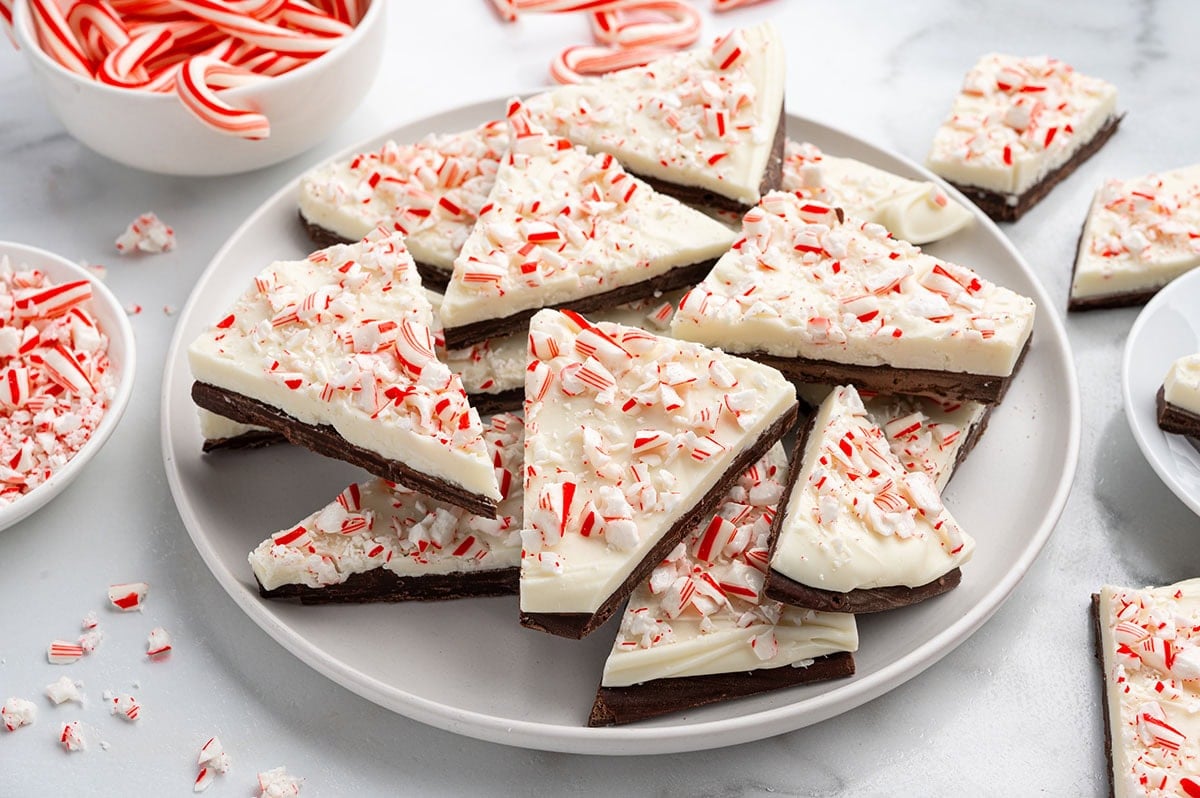 Broken pieces of peppermint bark sit on a white plate, topped with red and white candy bits.