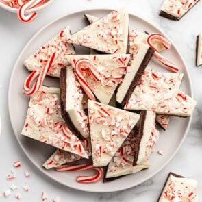 A white plate holds broken pieces of peppermint bark with crushed red and white candy on top.