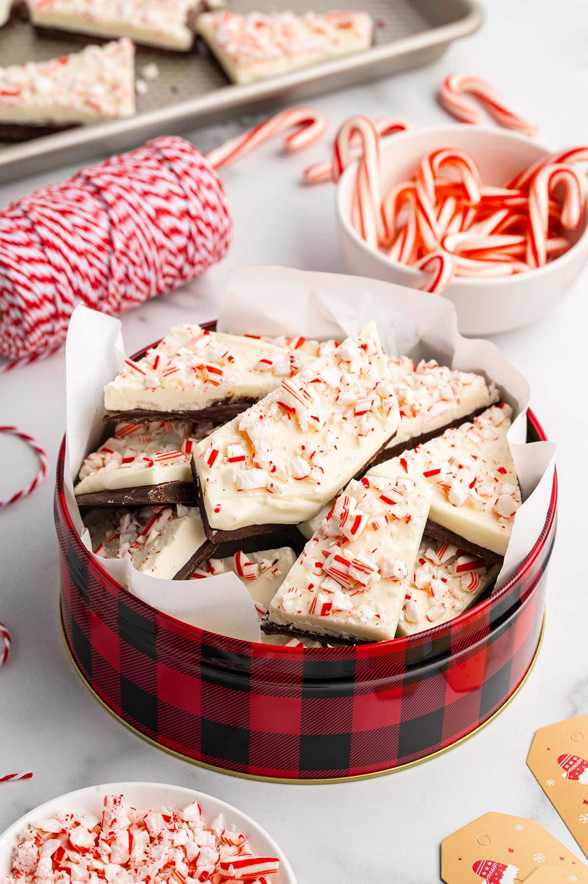 Homemade peppermint bark pieces in a red checkered tin, topped with crushed peppermint.