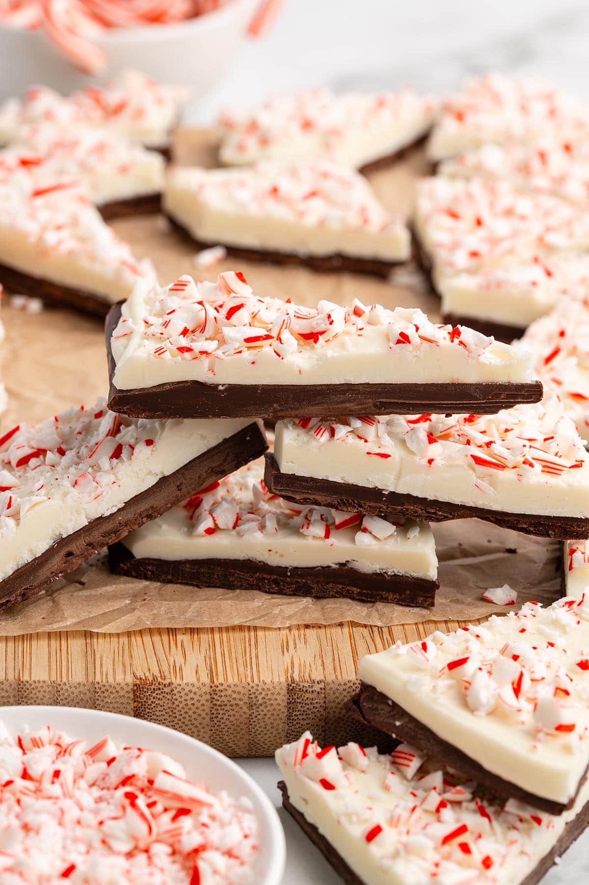 Stacked pieces of peppermint bark made with white chocolate and crushed candy canes on a wooden board.