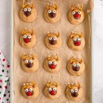 A baking sheet holds fresh reindeer peanut butter blossom cookies with pretzel antlers and candy eyes.