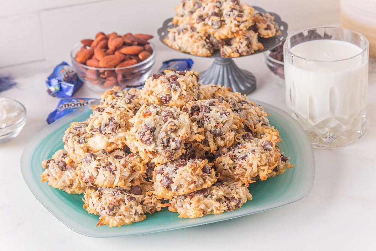 A stack of golden Almond Joy cookies on a teal plate, sprinkled with coconut and chocolate chunks.